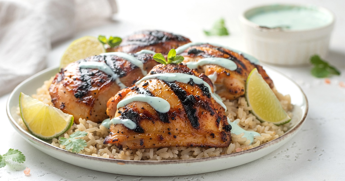 Grilled chicken on rice with green sauce and lime wedges.