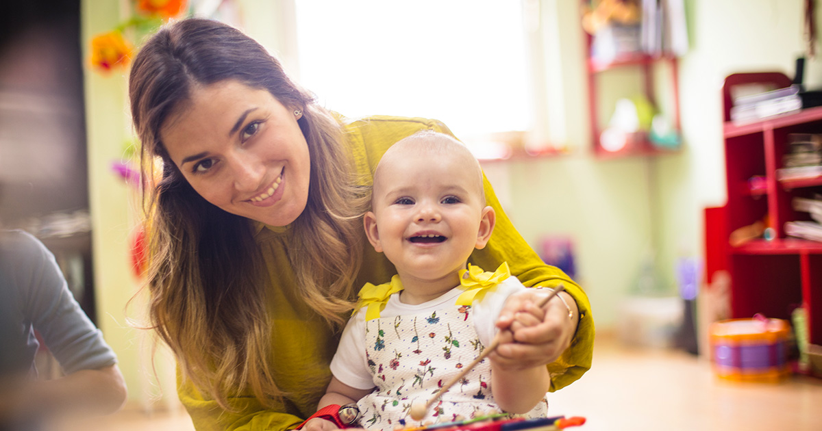 A teacher sitting with a baby playing with a xylophone.
